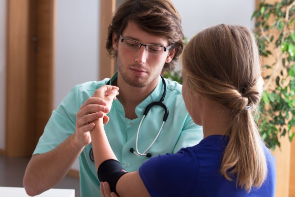 Orthopedist examining young woman's elbow in consulting room